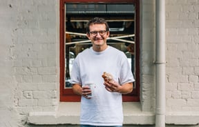 Ben Lenart holding a pastry and drink and smiling to camera.