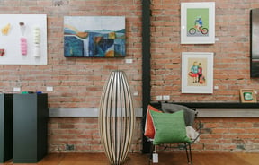 Art on display on a brick wall and a colourful chair on a wooden floor at 77 Art + Living in Fairlie.