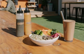 A bowl of healthy food sitting on a table alongside colourful smoothies.