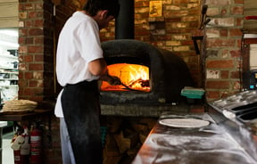 A chef putting pizza in the wood fired oven.