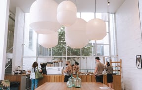 Large wooden tables with pendant paper lanterns above at Little Rosie, Auckland.