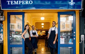 Two men and a woman standing in the bright blue entrance to Tempero restaurant in Auckland.