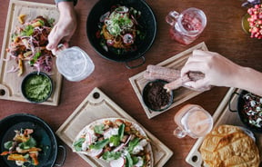 Hands reaching for different types of Mexican food on a table.e