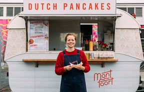 A woman holding dutch pancakes in front of a white caravan.