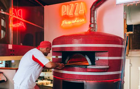 A man putting a pizza in a wood fired oven.