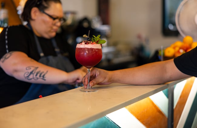 A hand holding a pink cocktail at the bar.