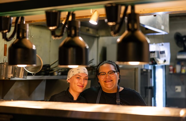Two chefs smiling at the camera from inside the restaurant kitchen at Anis.