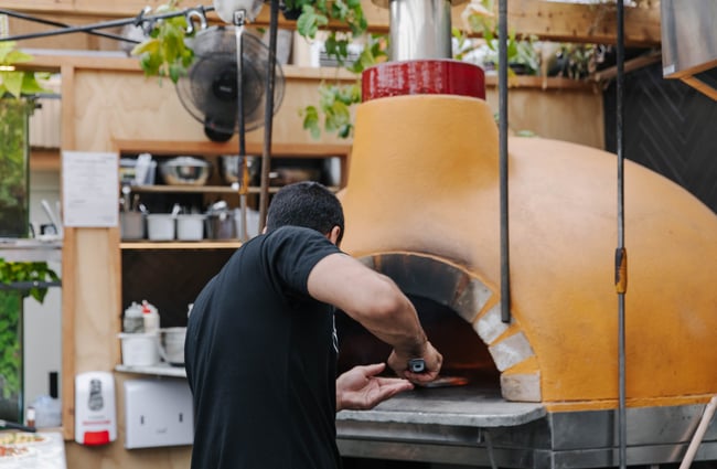 Man putting pizza into woodfire oven at Arbour in Lyttelton.
