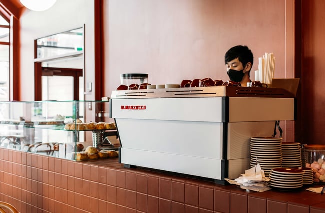 A masked barista making coffee behind the counter.