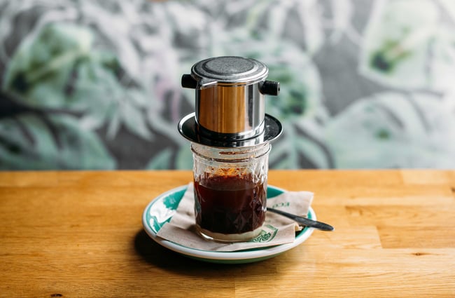 A form of coffee brewing with a silver canister on top of a glass.