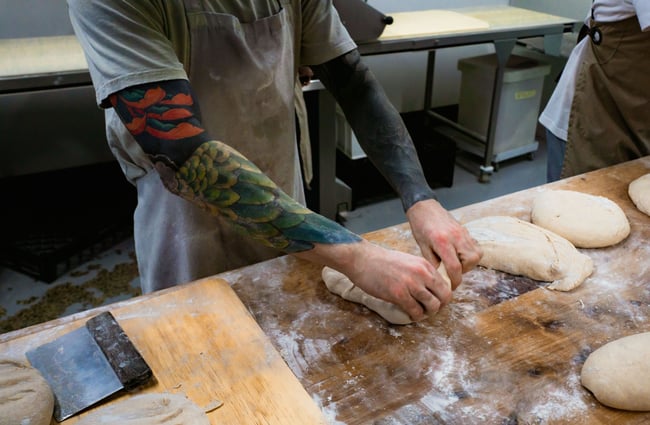 Tattooed arms of a baker making bread in the Bellbird Bakery kitchen in Christchurch.