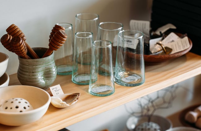 A close up of glasses and honey dippers on a shelf.