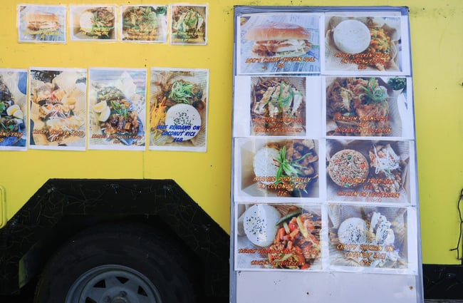 A large colourful menu leaned up against a food caravan.
