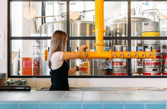 A female staff member pouring a beer in a brightly lit and colourful bar area.