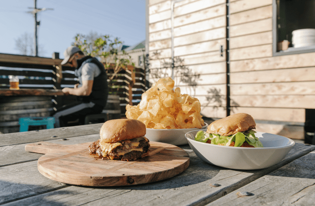 Two burgers and a bowl of chips on a wooden outside table.