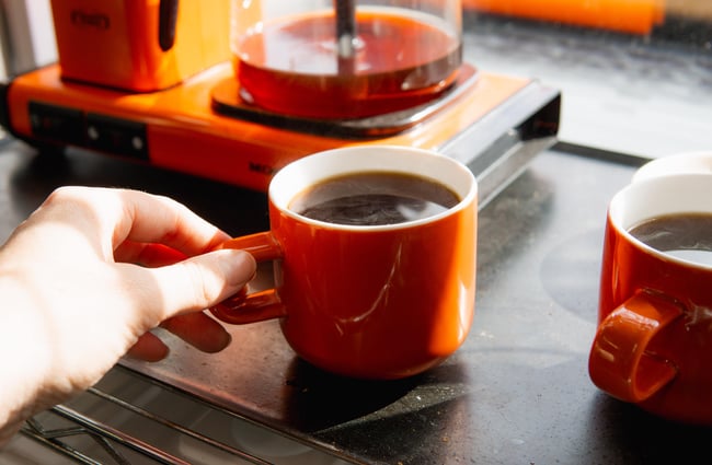 A hand holding an orange cup of black coffee.