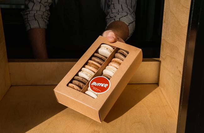 A box of chocolate macarons being handed out from a window.