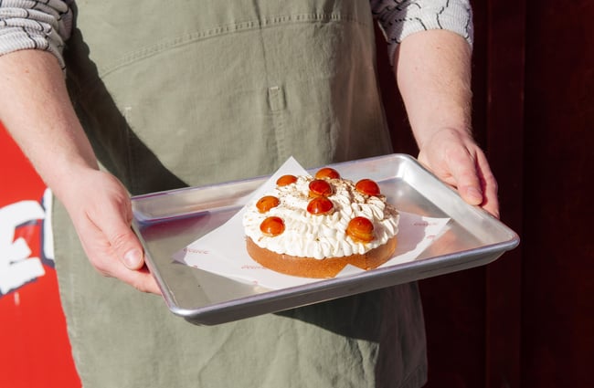 Hands holding a tray featuring a sponge cake topped with cream and strawberries.