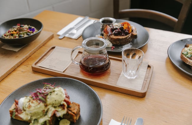 A close up of plates of brunch on a table alongside pour over coffee.