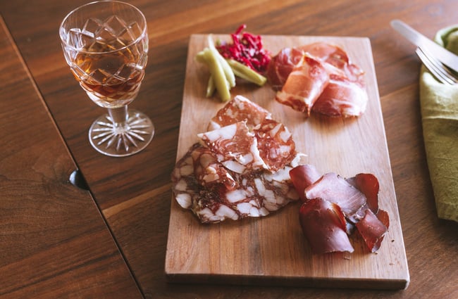 Cured meat platter on table with wine.