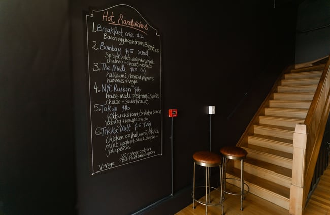 A chalkboard on a black wall promoting the sandwiches of the day.