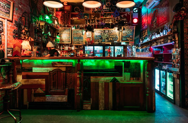 A green lit bar with a staff member working behind in the evening.