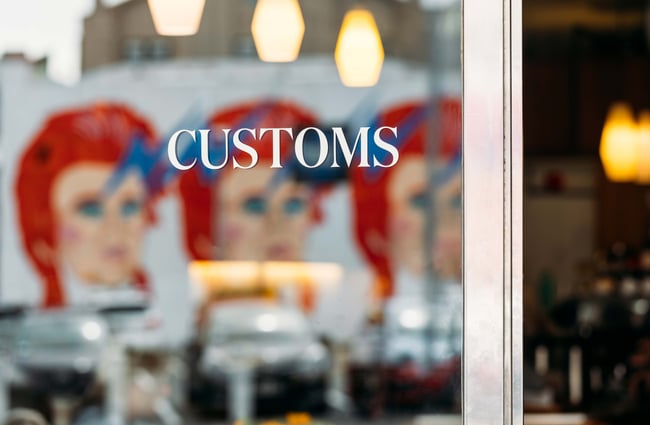 A close up of a white 'Customs' sign on a window.