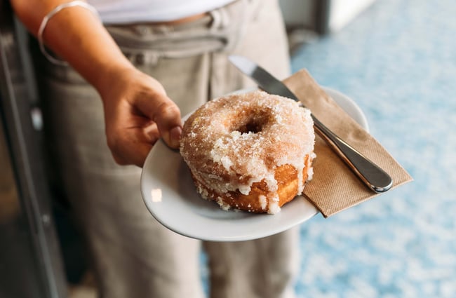 A close up of staff member holding a sugared donut.