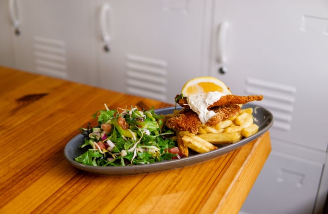 A plate of fish, chips and salad on a table.