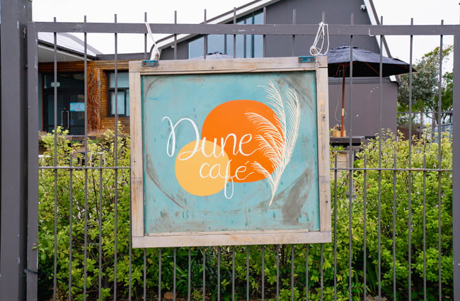 A sign that says 'Dune Cafe' sitting on a fence.