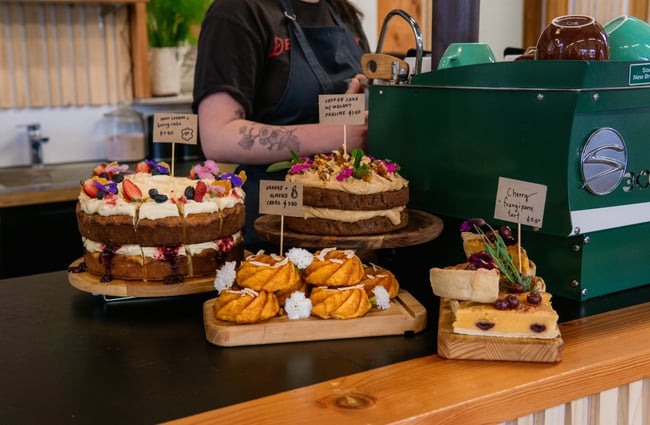 A close up of cakes on display on a cafe counter next to the coffee machine.