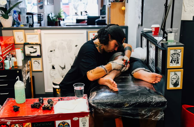 Man at work doing a tattoo on a leg.