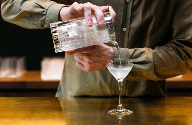 A man pouring gin into a martini glass.