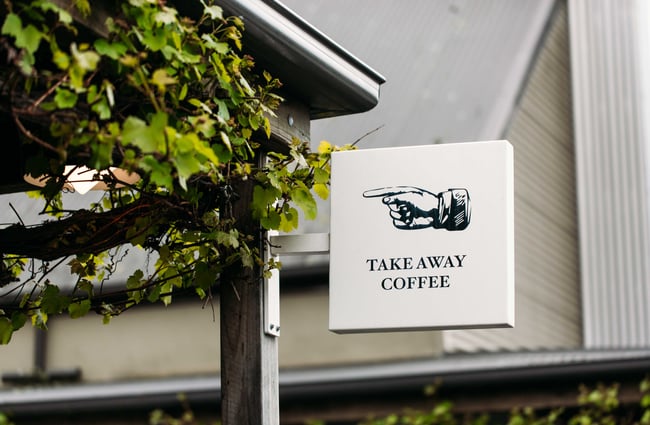 A takeaway coffee sign with a pointing hand attached to a roof.