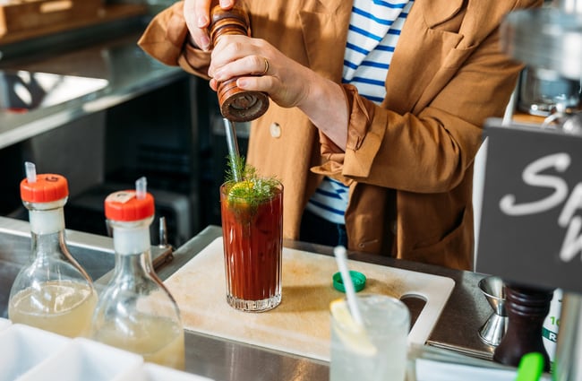 Close up of a woman cracking black pepper into a Bloody Mary cocktail behind the bar at Hayes Common in Hamilton.