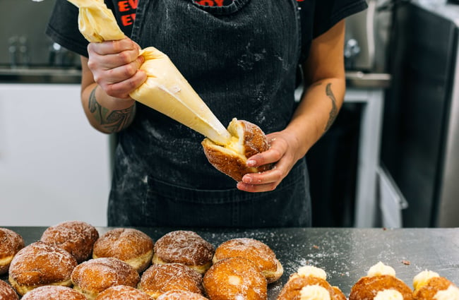 Person filling donuts with custard at Knead Artisan Donuts, New Plymouth.