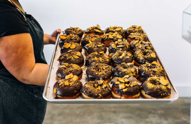 Person holding a tray of chocolate ganache donuts from Knead Artisan Donuts, New Plymouth.
