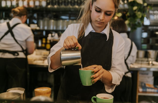 A female staff member making a coffee in a green cup.