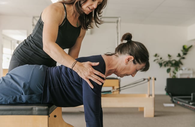 A pilates teacher holding on to the shoulders of a client.