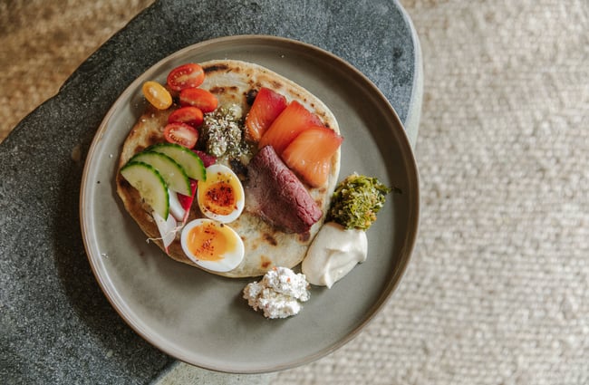 A flatlay of a plate of food including a naan bread, boiled egg and pickles.