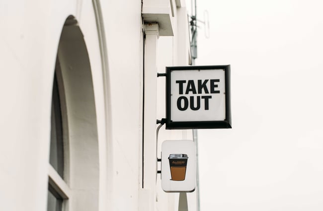 A black and white 'take out' sign on the exterior wall of Opera Kitchen.
