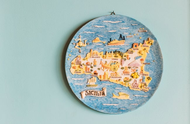 A close up of a round work of art featuring Sicily on a painted wall.