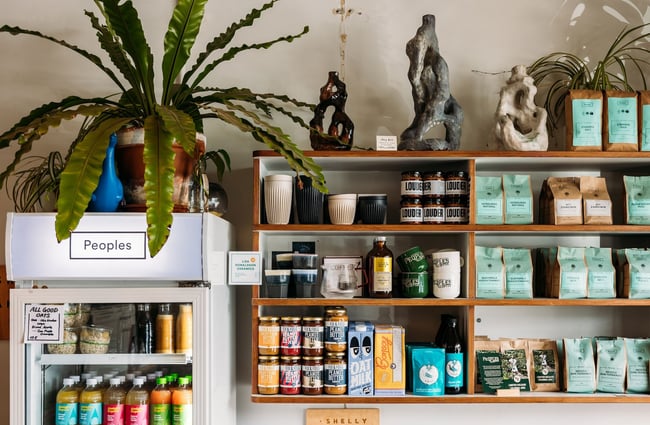 Display shelves mounted on the wall at Peoples Coffee in Newtown with peanut butter, coffee beans, ceramic takeaway mugs and more for sale.
