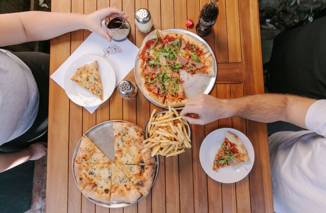 Birds eye view of two pizza and fries on wooden outdoor table.