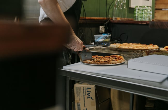 Chef using pizza cutter to slice freshly cooked pizza.