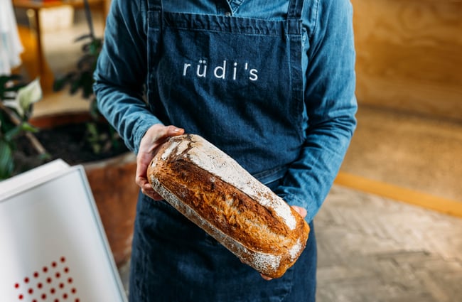 A person wearing a blue Rudi's apron holding a loaf of bread.