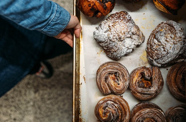 A hand pulling a tray with baked pastries.