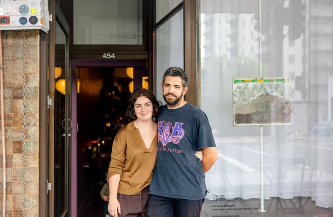 A man and woman posing for the camera outside their restaurant.