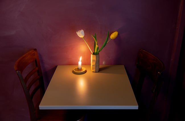A lit candle next to a vase of.flowers on a small restaurant table.