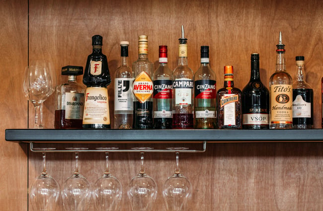 A close up of liquors on a floating shelf on a wall.